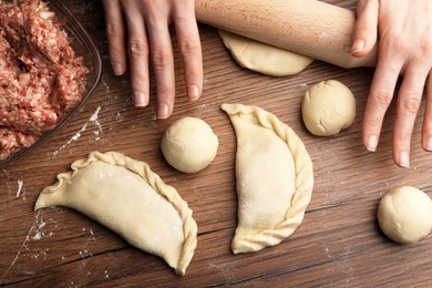 Photo of Woman rolling dough for chebureki on wooden table, flat lay