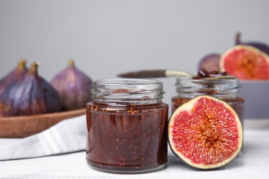 Glass jars of tasty sweet fig jam and fruits on white wooden table