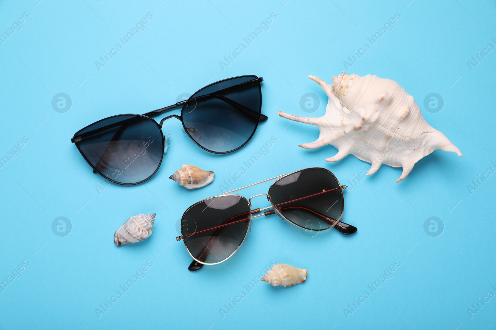 Photo of Stylish sunglasses and seashells on light blue background, flat lay