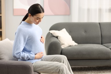 Photo of Pregnant young woman on armchair at home, space for text