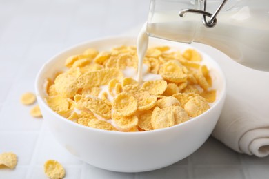 Photo of Breakfast cereal. Pouring milk into bowl with tasty corn flakes at white table, closeup