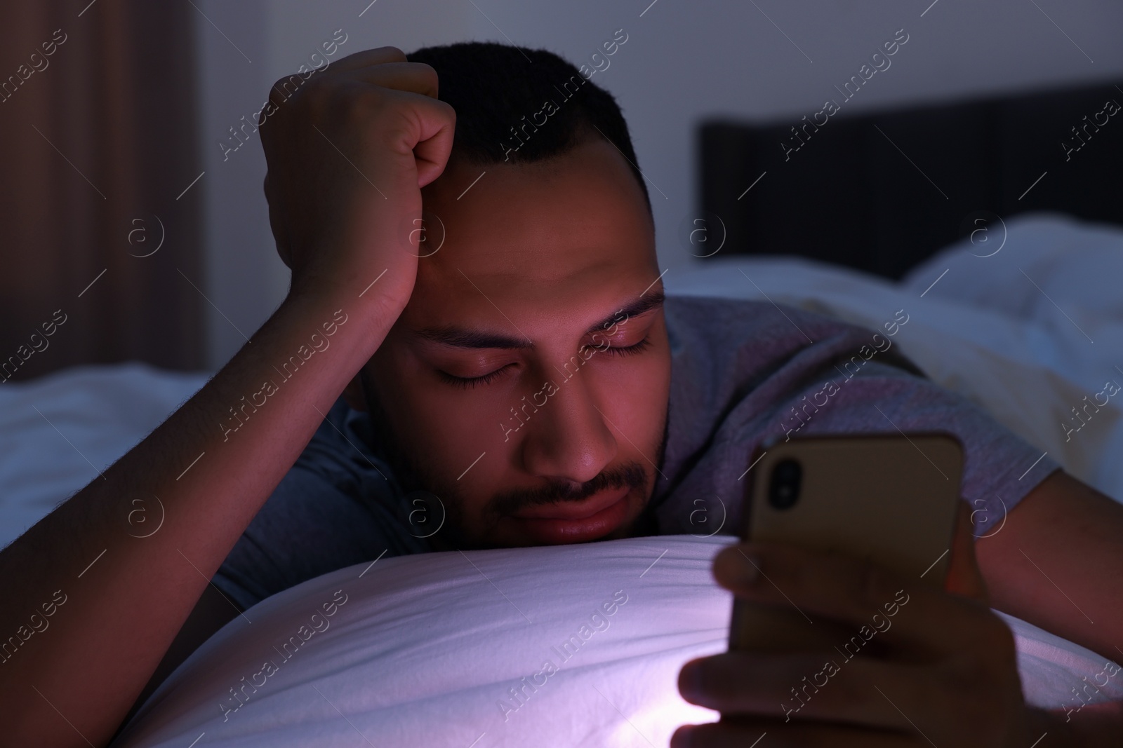 Photo of Young man sleeping while holding smartphone in bed at night. Internet addiction