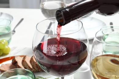 Photo of Pouring red wine into glass on table, closeup
