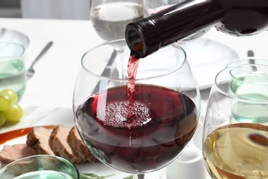 Pouring red wine into glass on table, closeup