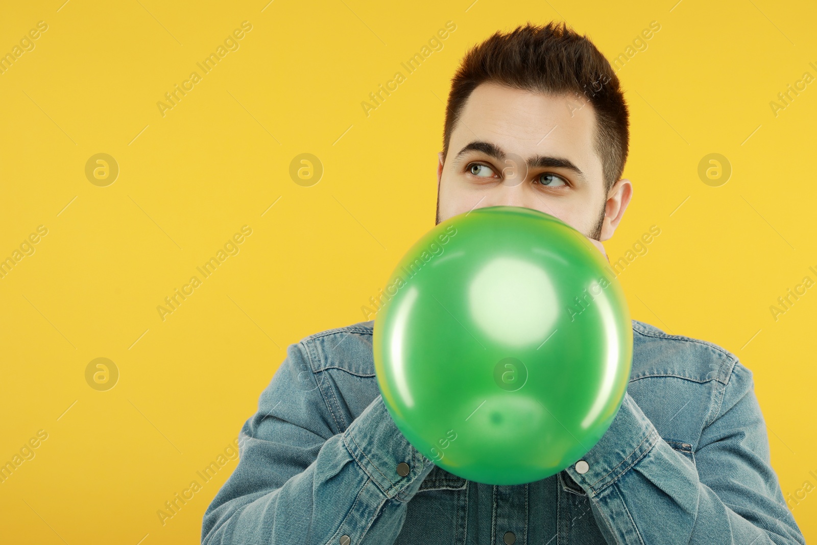 Photo of Man inflating bright balloon on yellow background, space for text