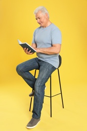 Senior man reading book on color background