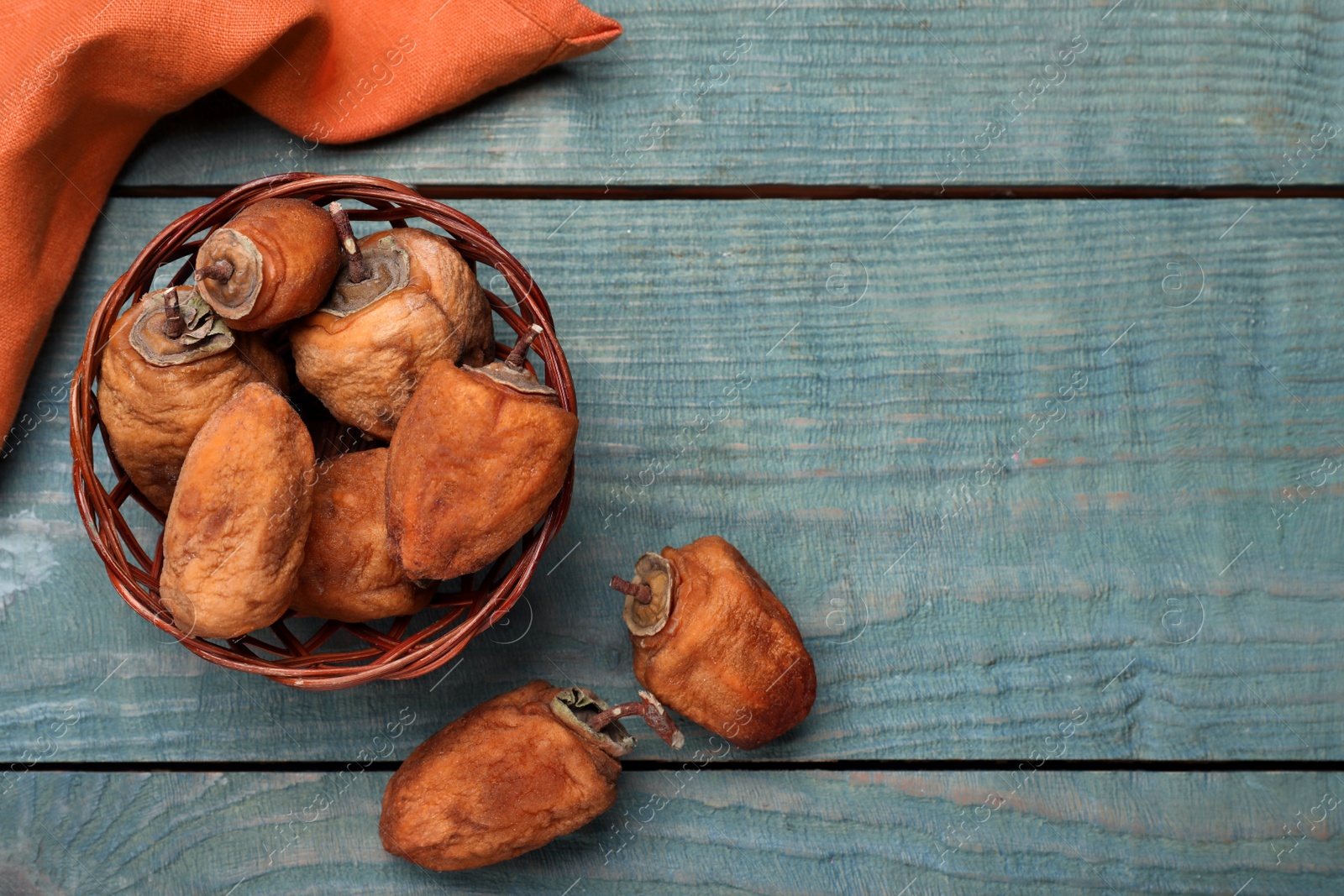 Photo of Wicker basket with tasty dried persimmon fruits on light blue wooden table, flat lay. Space for text