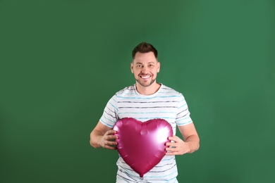 Portrait of young man with heart shaped balloon on color background