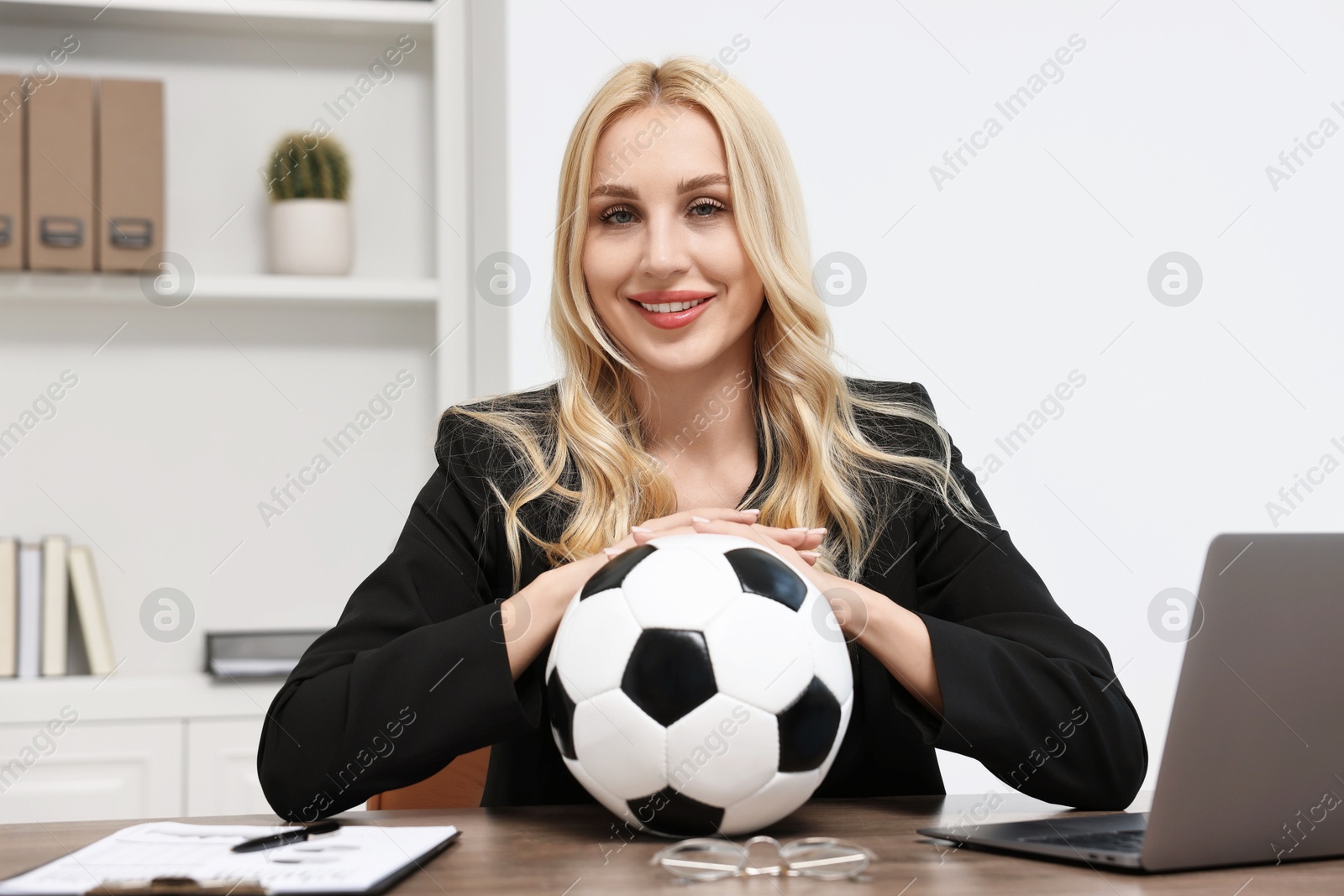 Photo of Happy woman with soccer ball at table in office