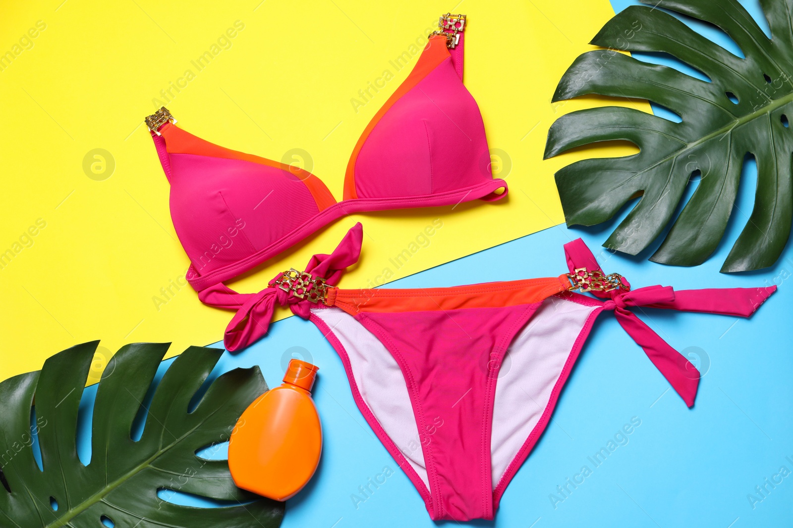 Photo of Stylish women's swimwear, sunscreen and green leaves on color background, flat lay