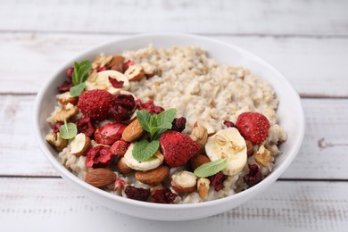 Photo of Delicious oatmeal with freeze dried berries, banana, nuts and mint on white wooden table, closeup