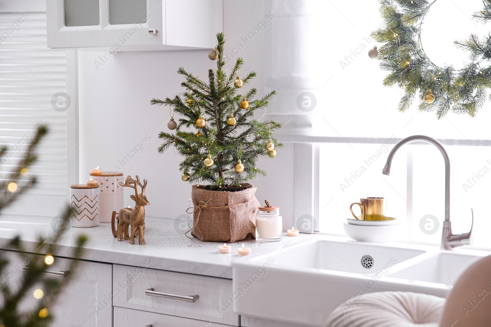 Photo of Small Christmas tree decorated with baubles and festive lights in kitchen