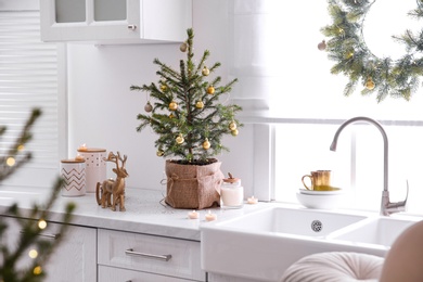 Photo of Small Christmas tree decorated with baubles and festive lights in kitchen