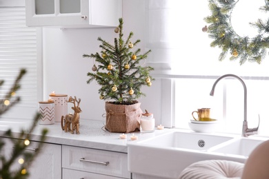 Small Christmas tree decorated with baubles and festive lights in kitchen