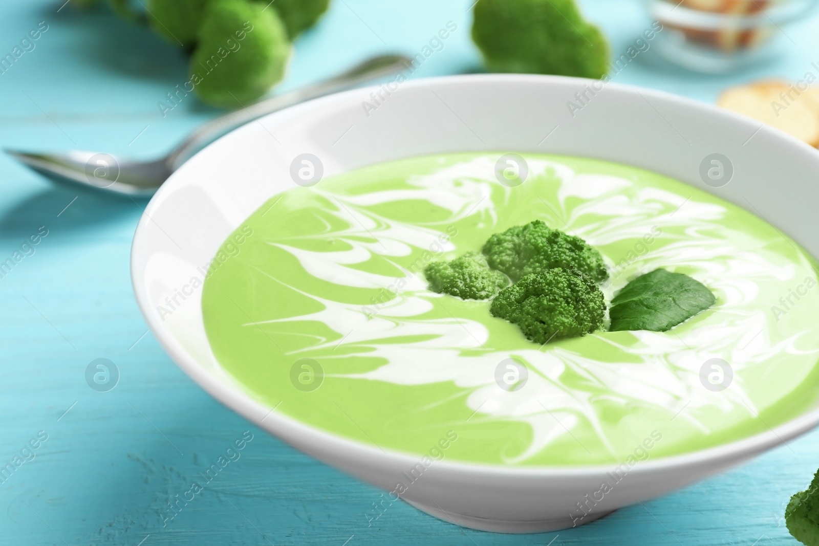 Photo of Bowl of cheese cream soup with broccoli served on blue wooden table, closeup