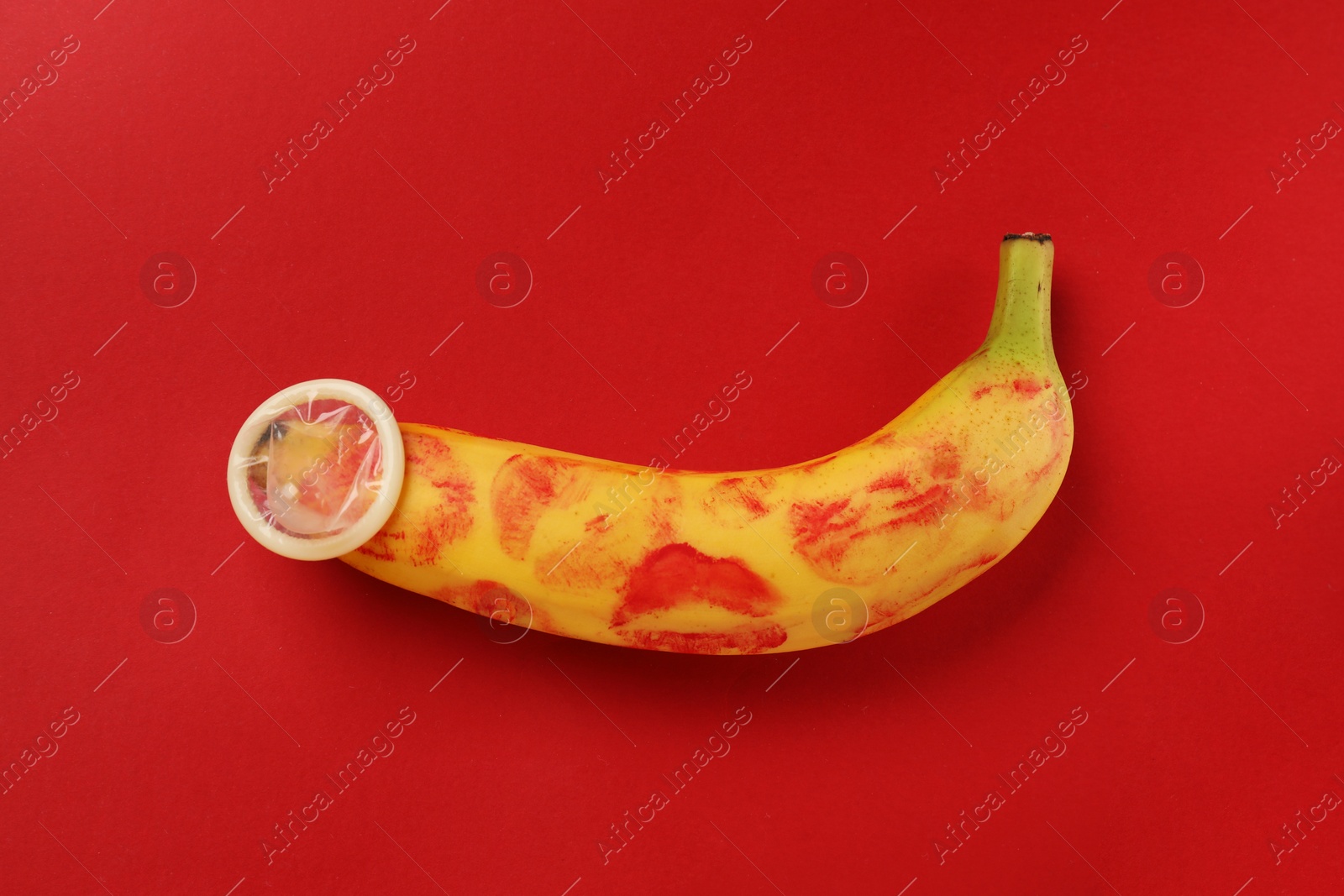 Photo of Banana with condom and lipstick marks on red background, top view. Safe sex concept