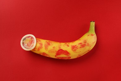 Photo of Banana with condom and lipstick marks on red background, top view. Safe sex concept