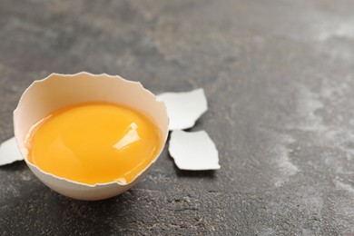 Photo of Cracked eggshell with raw yolk on grey table, closeup. Space for text