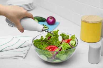 Photo of Woman adding cooking oil to delicious salad at table, closeup