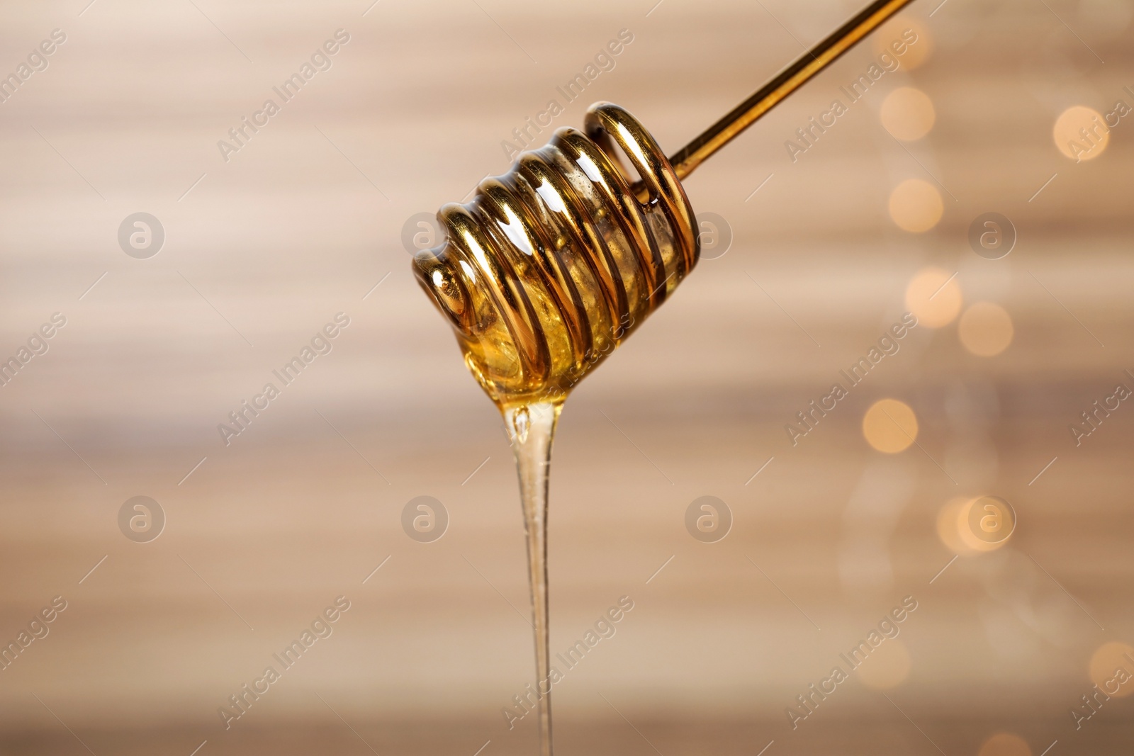 Photo of Dripping tasty honey from dipper on blurred background, closeup