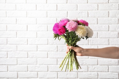 Woman holding beautiful aster flower bouquet against brick wall. Space for text