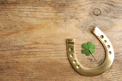 Photo of Clover leaf and horseshoe on wooden table, flat lay with space for text. St. Patrick's Day celebration