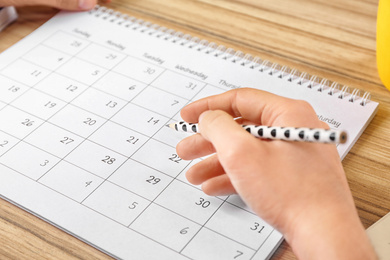 Photo of Woman with calendar at wooden table in office, closeup