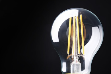 Photo of New modern lamp bulb on black background, closeup. Space for text