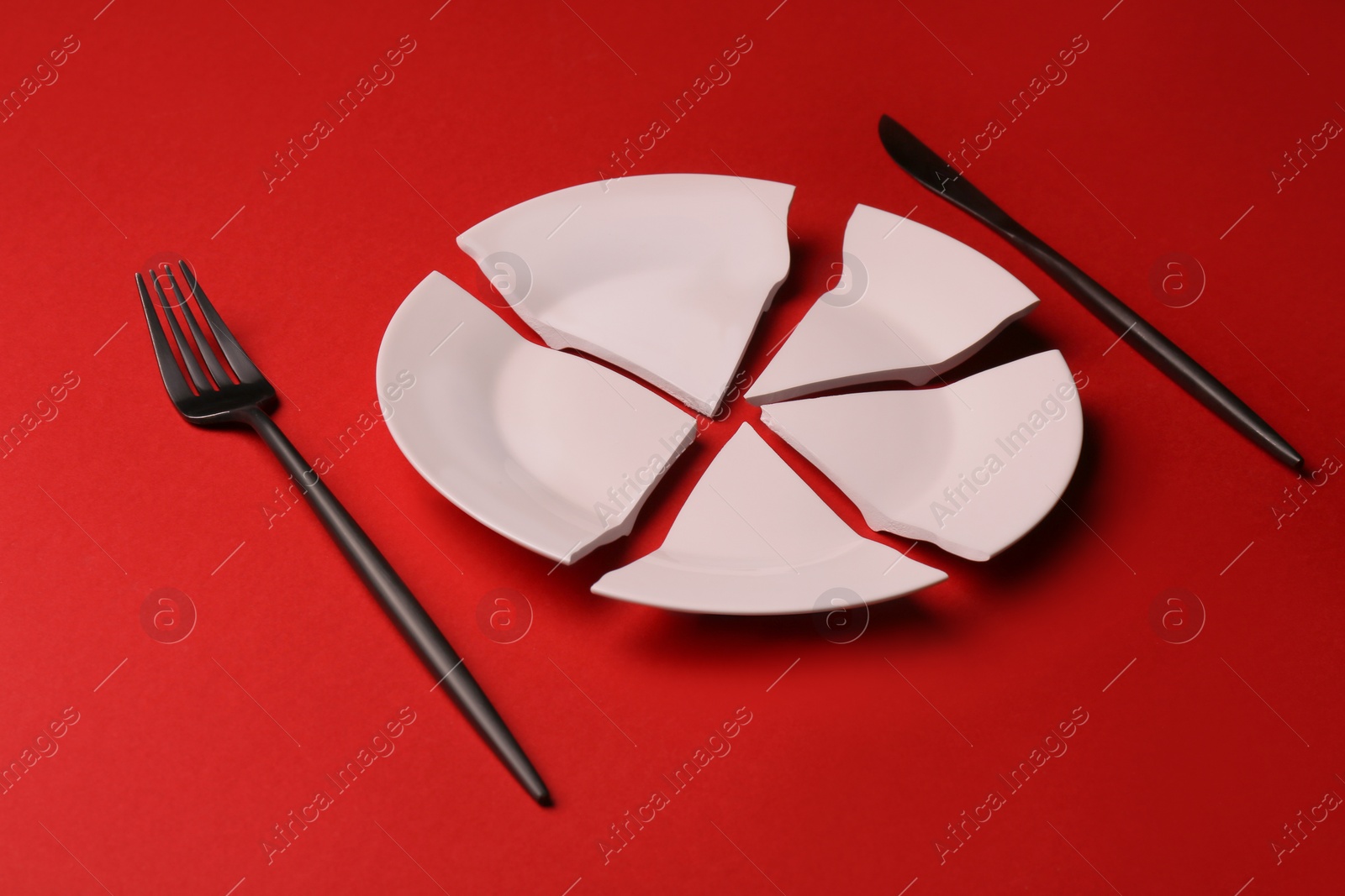 Photo of Pieces of broken ceramic plate and cutlery on red background