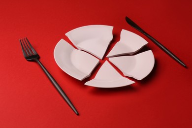 Photo of Pieces of broken ceramic plate and cutlery on red background