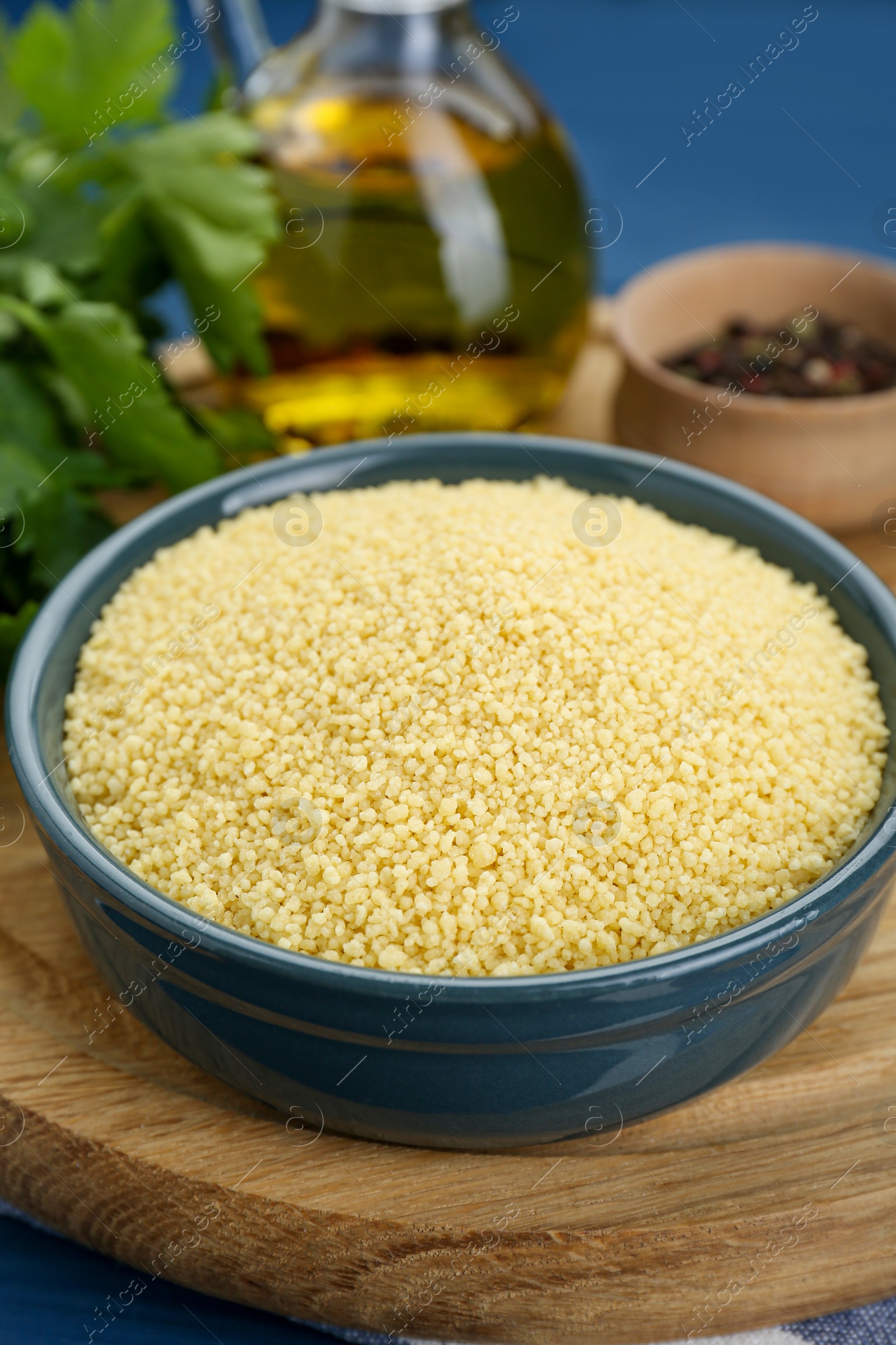 Photo of Bowl of raw couscous and ingredients on blue wooden table, closeup