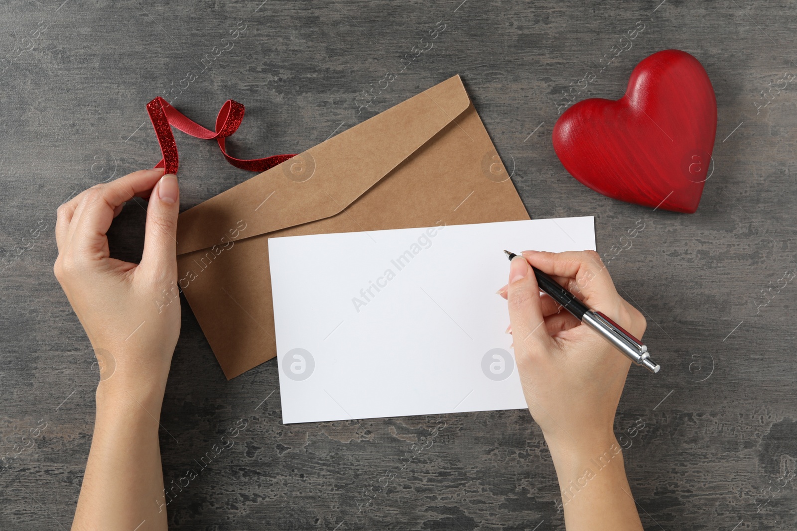 Photo of Woman writing on greeting blank card at grey stone table, top view. Valentine's day celebration