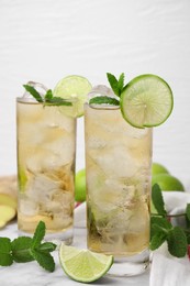 Photo of Glasses of tasty ginger ale with ice cubes and ingredients on white marble table, closeup
