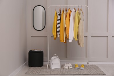 Rack with stylish women's clothes, backpack and shoes near light wall in dressing room