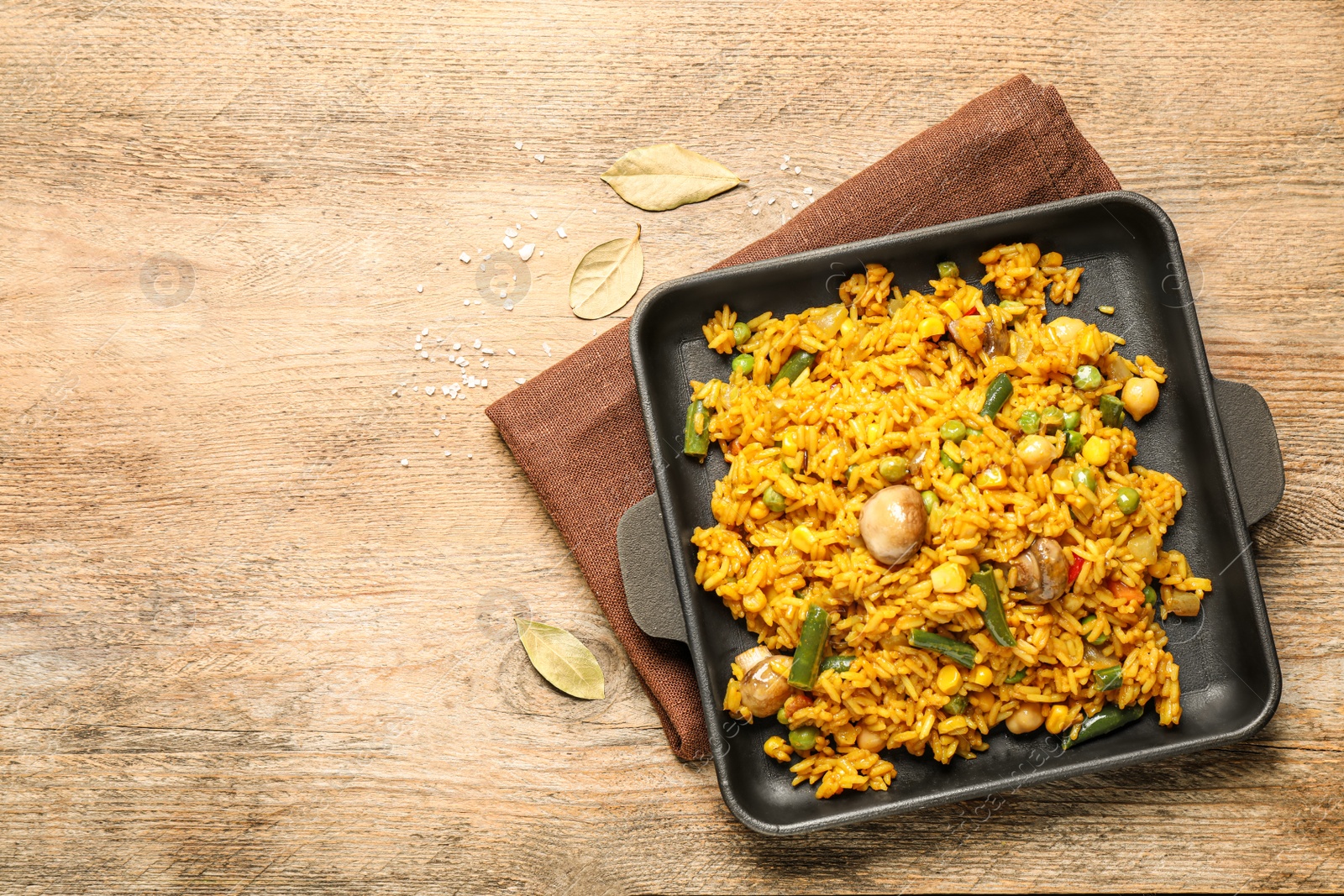 Photo of Delicious rice pilaf with vegetables on wooden table, top view. Space for text