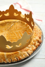 Photo of Traditional galette des Rois with paper crown on white wooden table, closeup