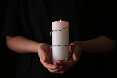 Photo of Woman holding candle with barbed wire on black background, closeup. Holocaust memory day
