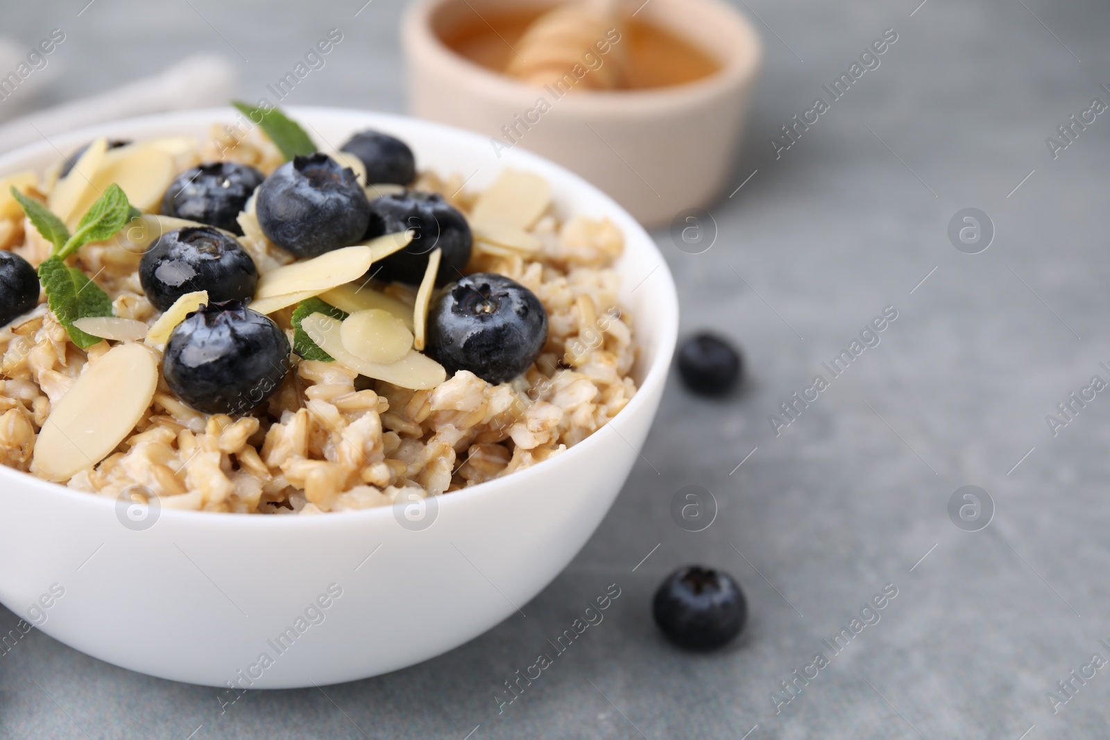 Photo of Tasty oatmeal with blueberries, mint and almond petals in bowl on grey table, closeup. Space for text