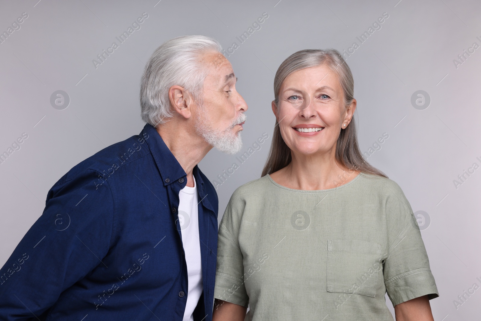 Photo of Senior man kissing his beloved woman on light grey background