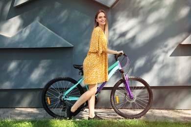 Happy young woman with bicycle near building outdoors