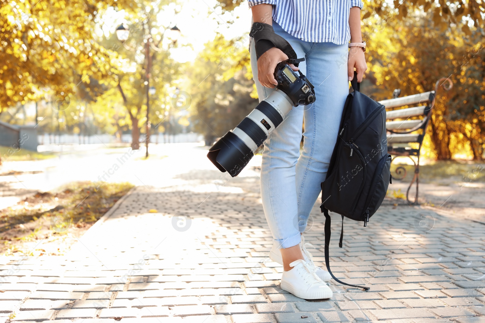 Photo of Young female photographer with professional camera and backpack in park. Space for text