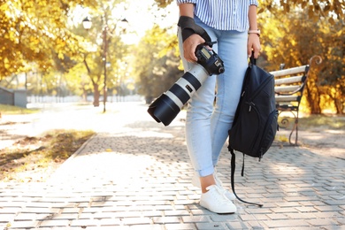 Young female photographer with professional camera and backpack in park. Space for text