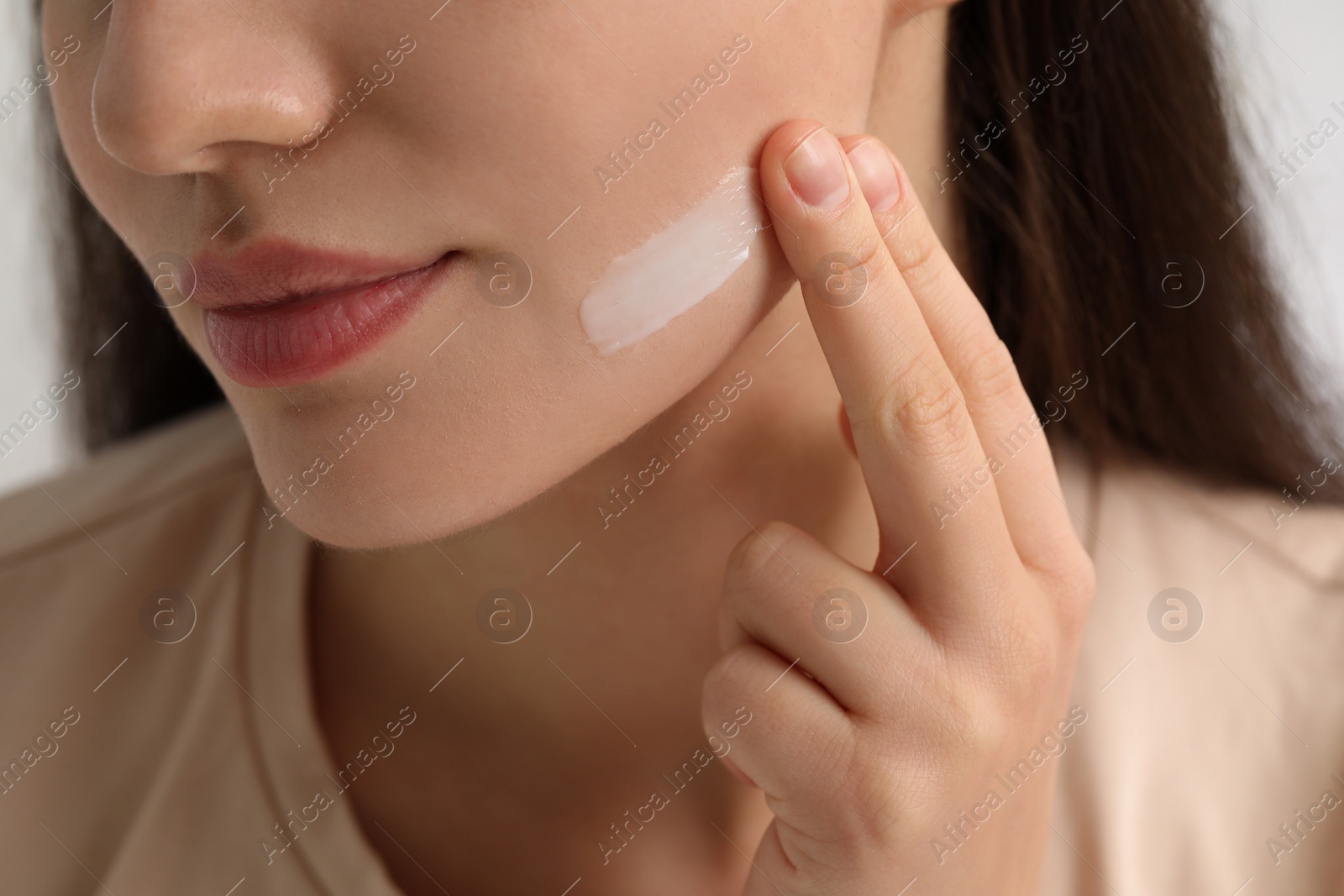 Photo of Young woman with dry skin applying cream onto her face on blurred background, closeup