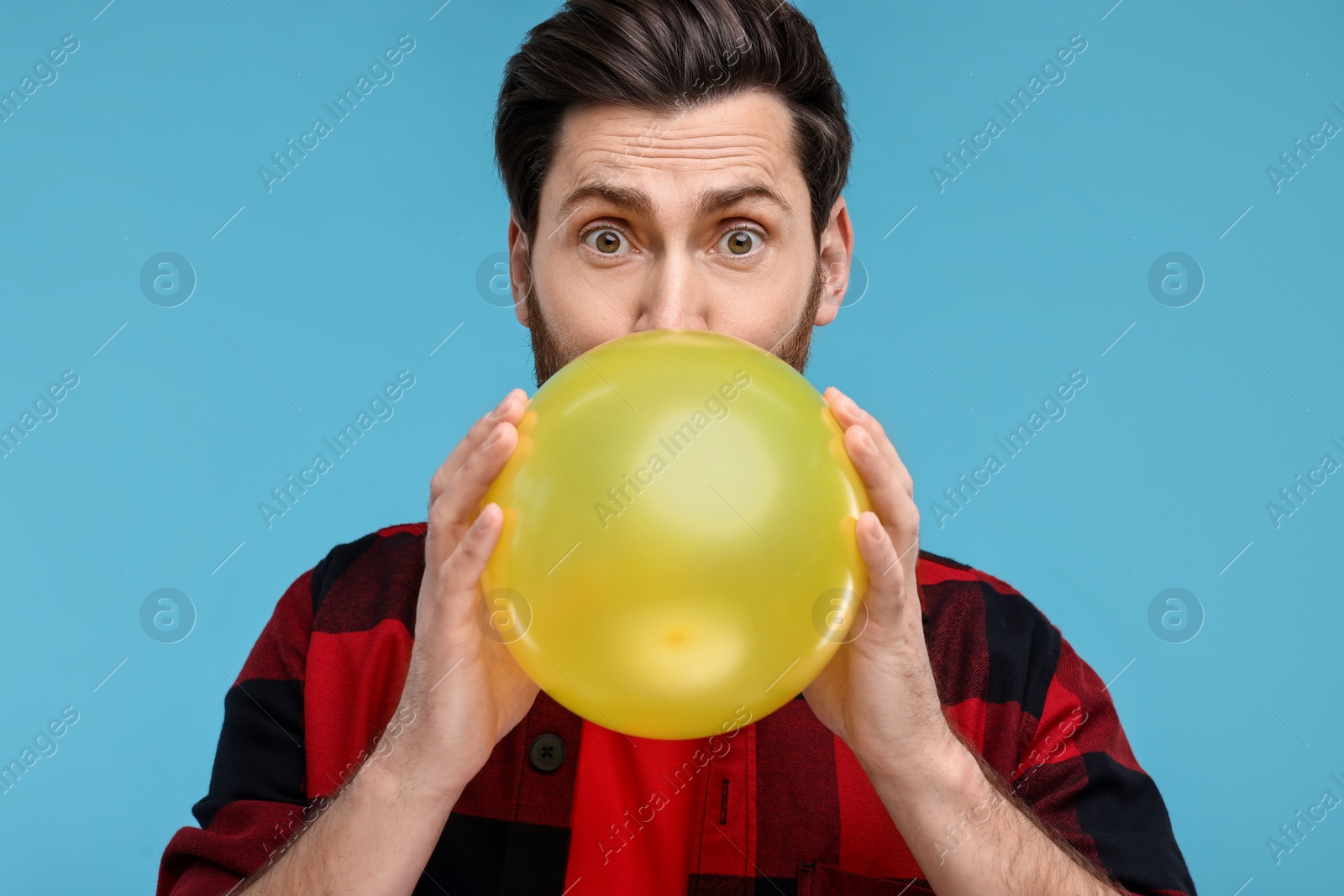 Photo of Man inflating yellow balloon on light blue background