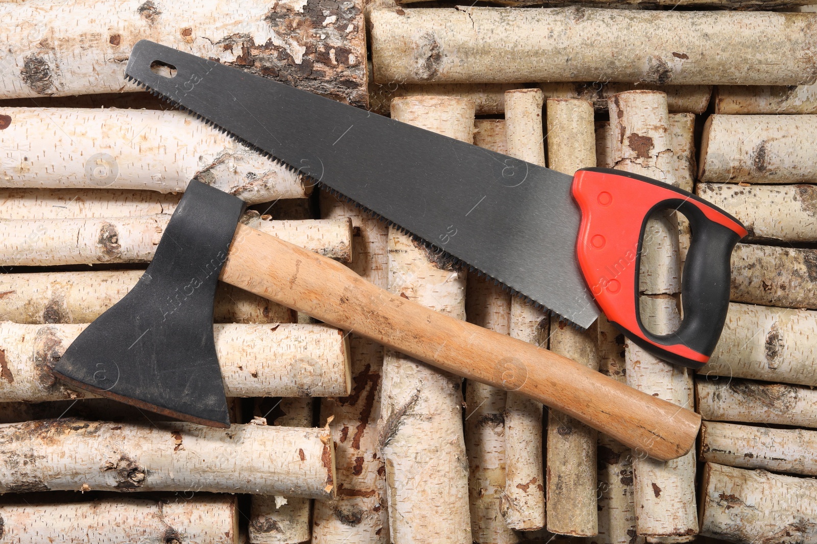 Photo of Saw with colorful handle and axe on firewood, flat lay