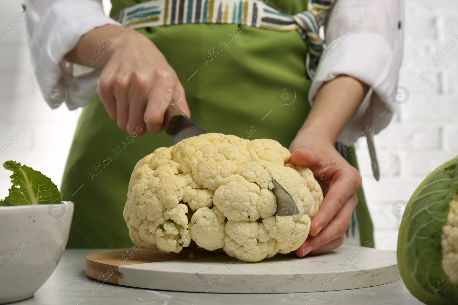 Photo of Woman cutting fresh cauliflower at light grey table, closeup