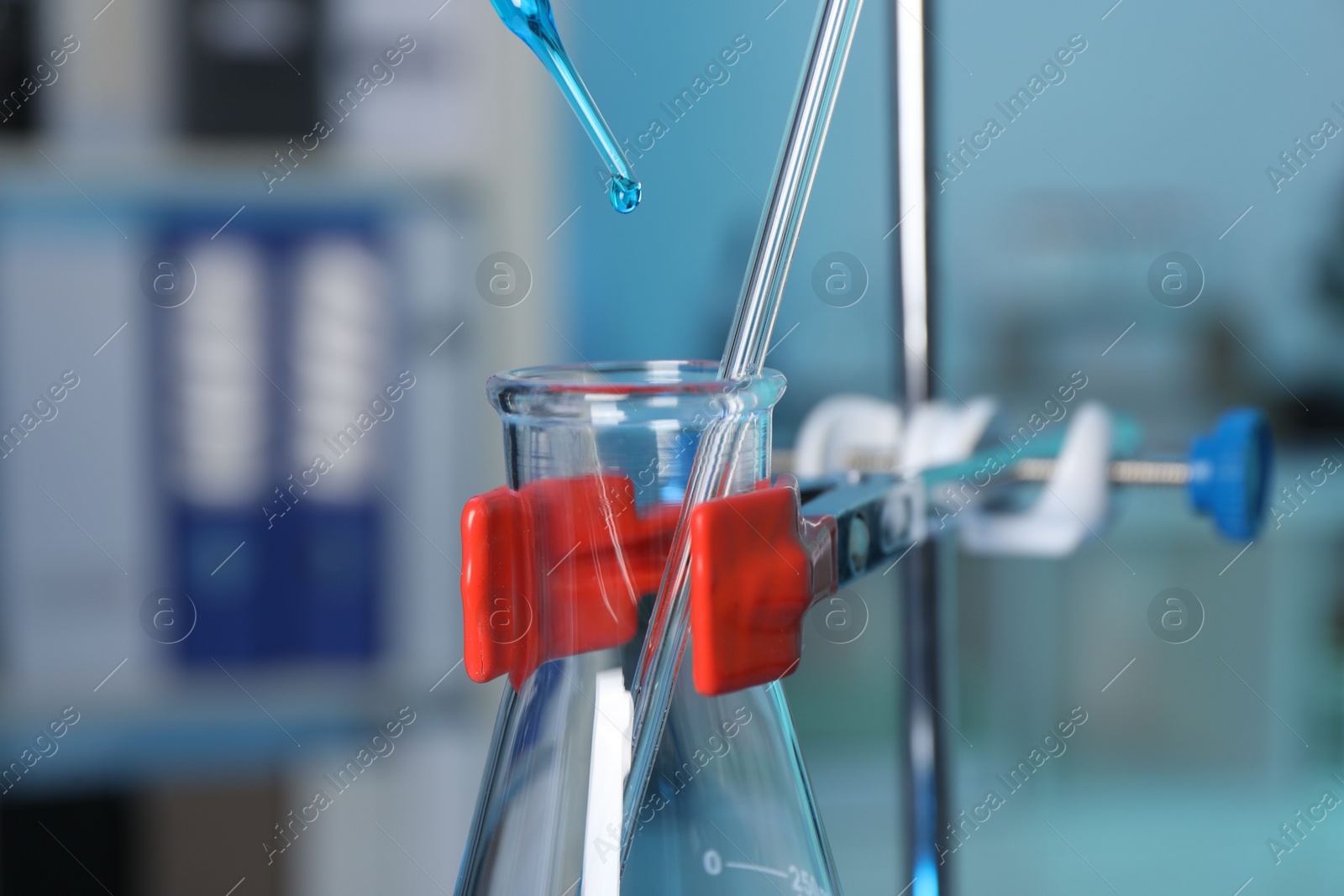 Photo of Laboratory analysis. Dripping blue liquid into flask on stand indoors, closeup