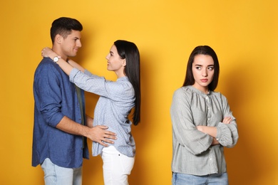 Unhappy woman feeling jealous while couple spending time together on yellow background