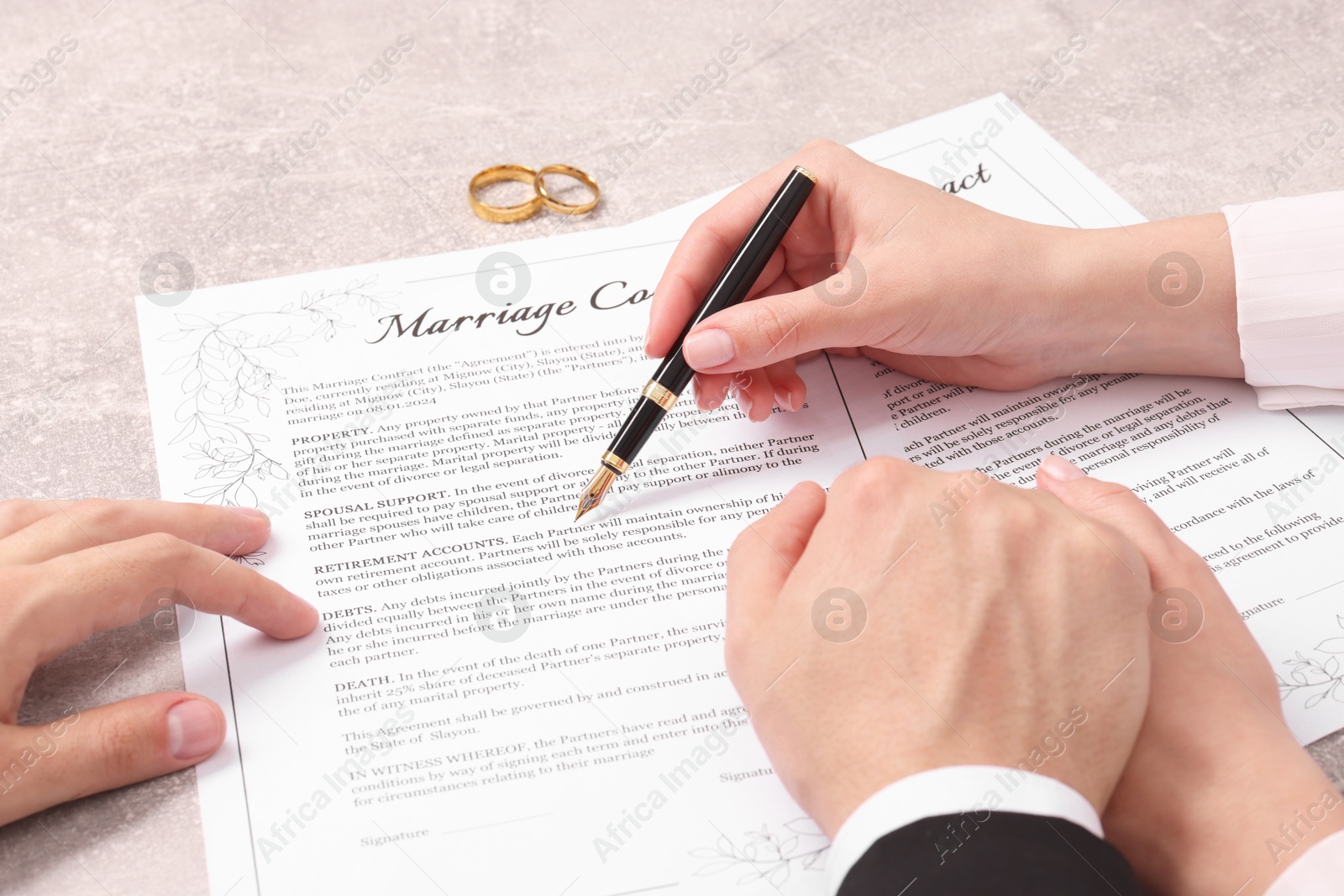 Photo of Man and woman signing marriage contract at light grey table, closeup