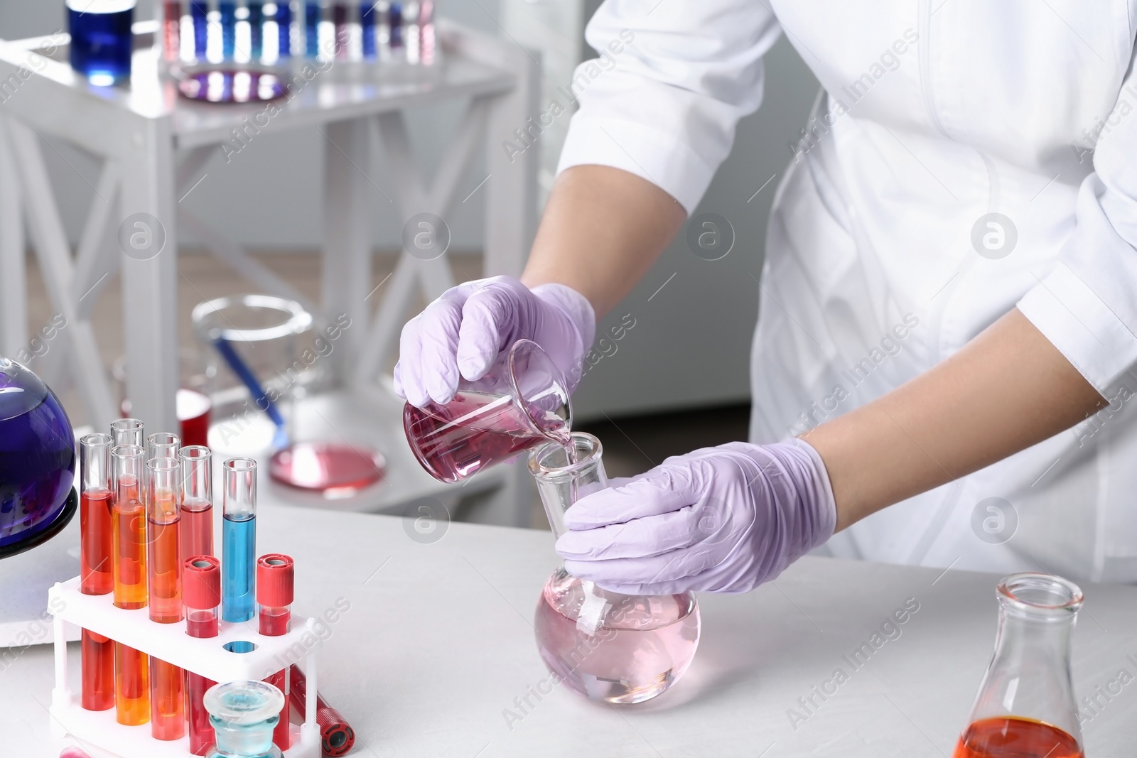 Photo of Scientist pouring reagent into flask at table in chemistry laboratory